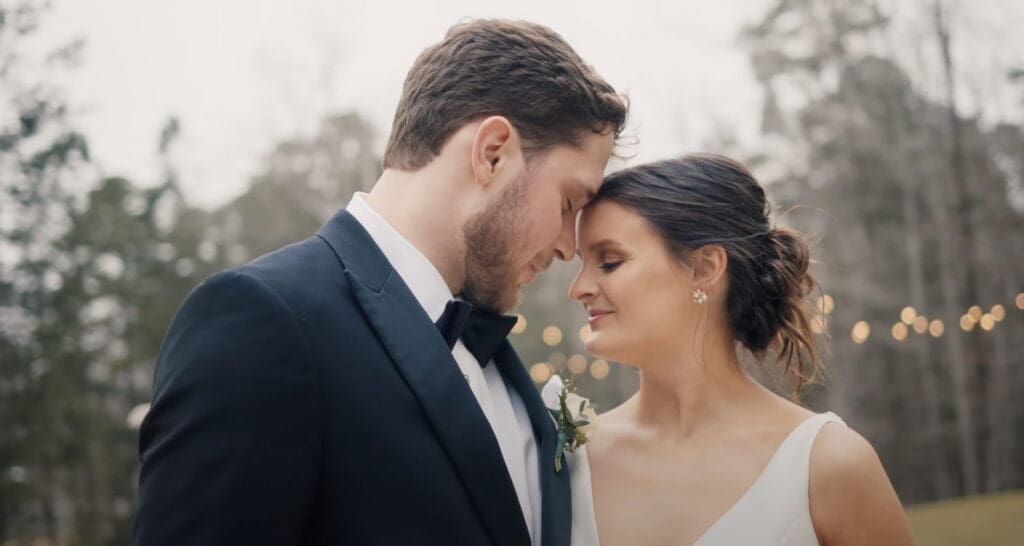 Bride and groom stand close with foreheads touching during an outdoor wedding portrait, showing an intimate moment often featured in wedding video packages.