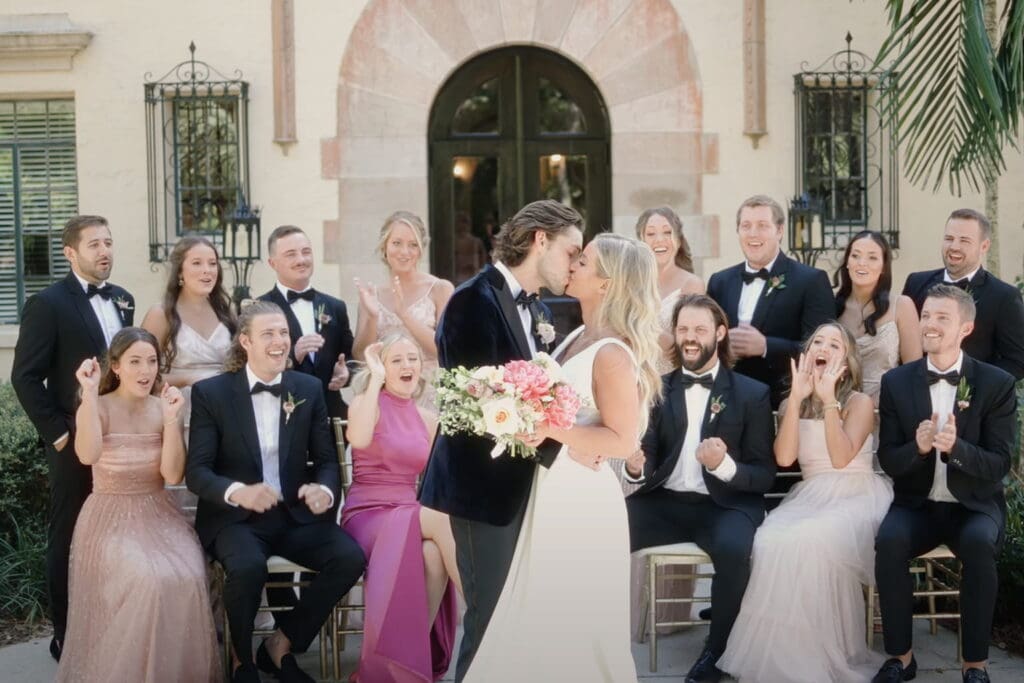 Bride and groom kiss during a joyful wedding celebration while friends and family cheer, capturing a moment often shared in wedding toasts