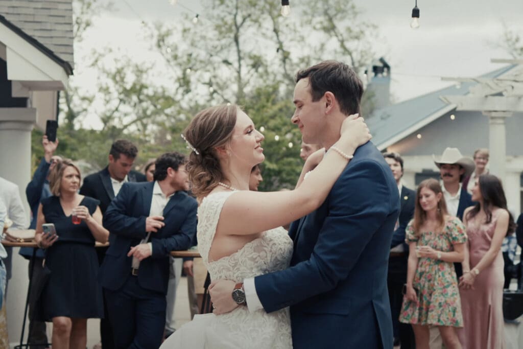 Couple dances at an outdoor reception while guests wear semi formal outfits, helpful example of what to wear to a semi formal wedding