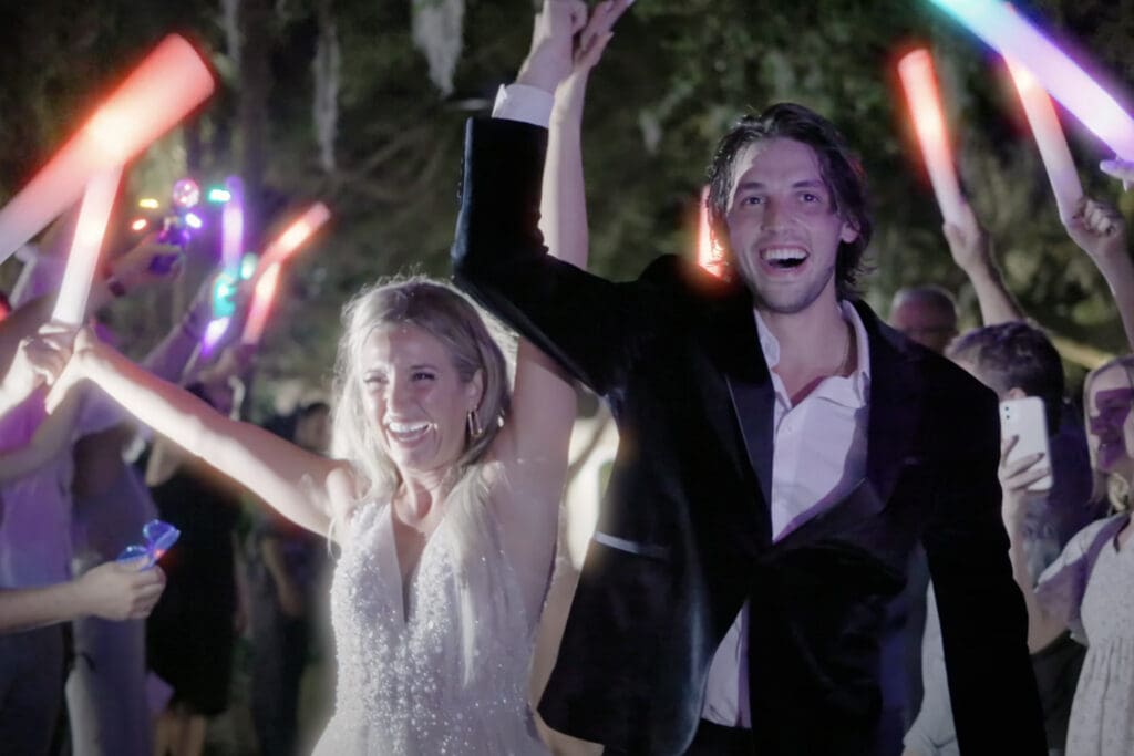 Bride in white dress and groom in black suit celebrate during a sparkler exit, example of formal wedding attire for guests asking what to wear to a wedding