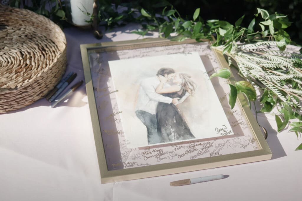 Creative engagement photo outfits display featuring a framed illustration of a couple embracing, surrounded by greenery, pens, and a guest book setup on a table.
